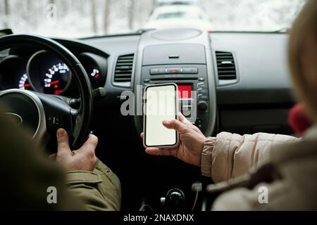 Nahaufnahme einer Seniorin, die ihr Smartphone mit leerem Bildschirm hielt, während sie im Auto neben ihrem Mann saß und während der Fahrt das Lenkrad hielt Stockfoto