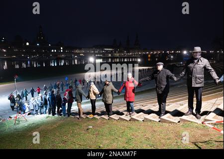 Dresden, Deutschland. 13. Februar 2023. Die Zerstörung der Stadt während des Zweiten Weltkriegs wird mit einer menschlichen Kette am Königsufer geehrt. Am 13. Februar erinnert die Hauptstadt Dresden an die Zerstörung der Stadt im Zweiten Weltkrieg vor 78 Jahren. Am 13. Und 14. Februar 1945 reduzierten die alliierten Bomber das Zentrum der Stadt auf der Elbe in Schutt und Asche. Bis zu 25.000 Menschen haben ihr Leben verloren. Kredit: Sebastian Kahnert/dpa/Alamy Live News Stockfoto