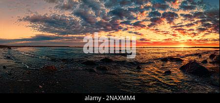 Die goldene Sonne fällt unter den Horizont und strahlt ein warmes Licht über den Ozean, die Wellen stürzen ab und der Himmel verwandelt sich in eine Leinwand in Orange-, Pink- und Lila-Tönen Stockfoto