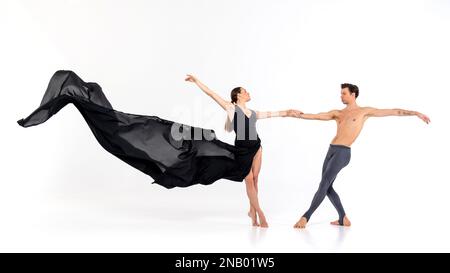 Weibliche Balletttänzerin mit einem langen fließenden schwarzen Kleid, die mit ihrem Partner isoliert auf weißem Hintergrund tanzt Stockfoto