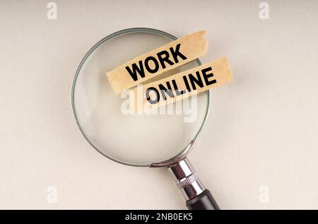 Auf dem Vergrößerungsglas befinden sich Papierstreifen mit der Aufschrift „Work Online“ (Online arbeiten). Stockfoto