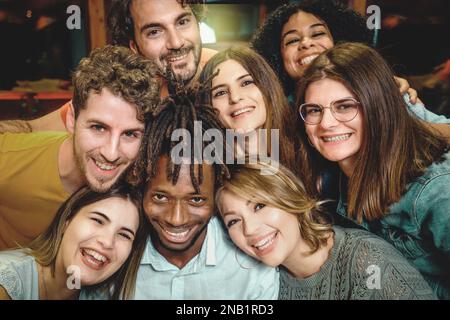 Ein Bild mit einer Nahaufnahme von 8 lächelnden und fröhlichen multikulturellen jungen Menschen, die ihre Köpfe für ein Gruppenfoto versammeln. Stockfoto