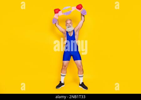 Porträt über die gesamte Länge des flippigen Mannes mit positivem Alter Tragen Sie Boxhandschuhe mit erhobenen Armen Halten Sie den weichen Champion-Gürtel isoliert auf gelbem Hintergrund Stockfoto