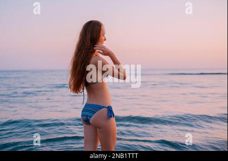 Silhouette Happy Beautiful Young Woman ein langes Haar in einem Badeanzug, die Oberarme am Strand am Sonnenuntergang an der Adria in Montenegro Stockfoto