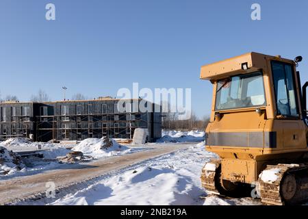 Ein Bulldozer auf einer Baustelle im Winter vor dem Hintergrund modularer Gebäude. Baugewerbekonzept Stockfoto