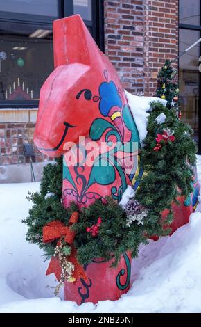 Farbenfrohes rotes schwedisches Dalapferd mit einem wunderschönen Weihnachtskranz an einem Wintertag in Scandia, Minnesota, USA. Stockfoto