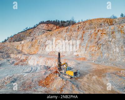Gelber Bagger gräbt Steine im Steinbruch und erledigt die ganze harte Arbeit Stockfoto