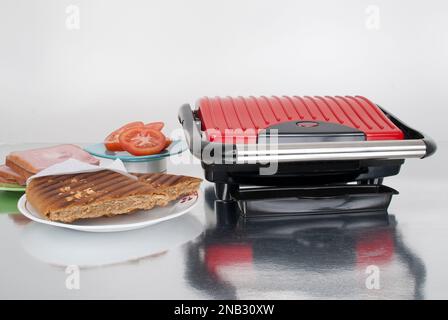 Haushaltsgerät rote Panini-Maschine; Foto auf neutralem Hintergrund. Stockfoto