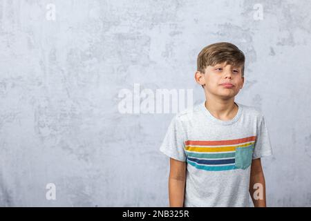 Ein süßer kleiner Junge mit Autismus in einem Studio, der ein schmieriges Gesicht mit geschlossenen Augen macht Stockfoto