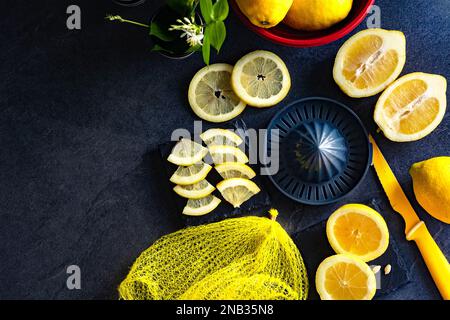 Elegantes Hintergrunddesign aus Zitronen und Zitronenscheiben mit Quetschpresse und Messer auf dunkler oder schwarzer Zement- oder Steinoberfläche.Draufsicht mit Kopierraum. Stockfoto