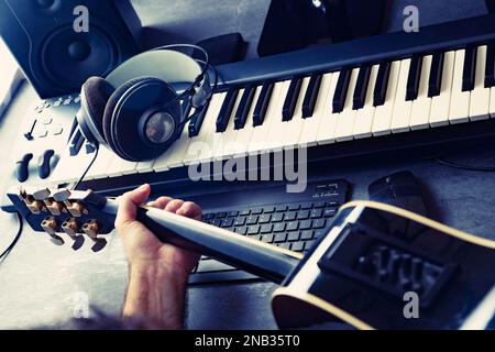 Tastatur oder Synthesizer und Gitarrist mit Kopfhörern und Soundkarte. Computeraufnahme- und Musikproduktionskonzept. Musik und digitales Studio. Stockfoto