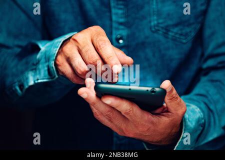 Senden einer sms und Teilen von Inhalten in sozialen Netzwerken aus dem Haus.Nahaufnahme der Hand eines Mannes, der sein Smartphone hält. Stockfoto