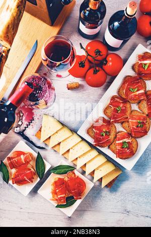 Vorspeisen mit iberischem Schinken mit einem Glas Wein, reifen Tomaten und Kuhkäse auf weißem Holzhintergrund. Stockfoto