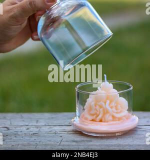 Eine Hand öffnet ein Glasgefäß mit einer dekorativen rosafarbenen Kerze Stockfoto