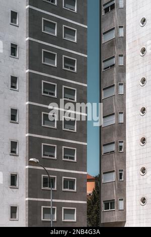 Vertikale Aufnahme von zwei modernen, strukturierten, grauen Wohngebäuden, wobei der enge Raum dazwischen einen hohen Streifen zeigt, der passiert Stockfoto