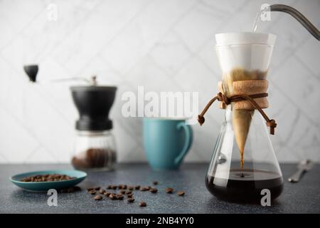 Zubereitung von Pour-Over-Kaffee in einem Glasbehälter auf einer Arbeitsfläche aus sauberem Stein mit weißem Marmorblitz Stockfoto