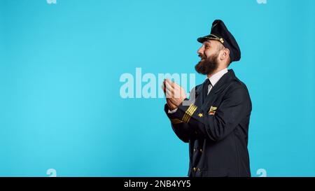 Männlicher Pilot applaudiert und jubelt vor der Kamera, gratuliert und klatscht im Studio. Flugzeugpilot in Fluguniform mit fröhlichen Emotionen und Standing Ovation Schild. Stockfoto