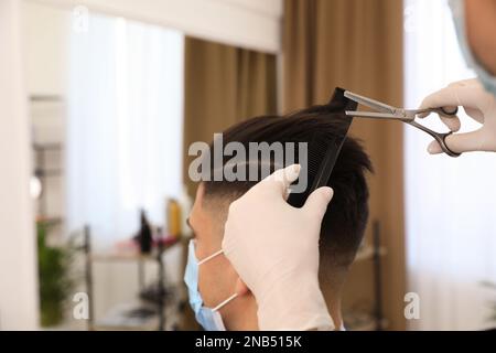 Professioneller Stylist, der mit einem Kunden im Salon zusammenarbeitet, Nahaufnahme. Friseurdienste während der Coronavirus-Quarantäne Stockfoto