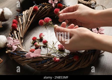 Florist, der Kranz mit getrockneten Blumen am Holztisch macht, Nahaufnahme Stockfoto