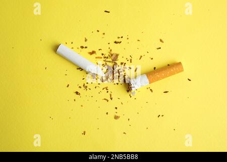Gebrochene Zigarette auf gelbem Hintergrund, flach gelegt. Raucherentwöhnungskonzept Stockfoto