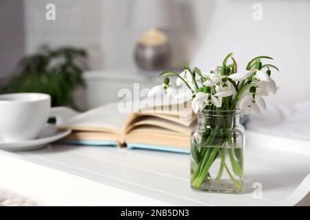 Wunderschöne Schneetropfen, Buch und eine Tasse Kaffee auf dem Tablett im Schlafzimmer. Platz für Text Stockfoto