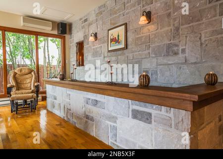 Karamellfarbener Ledersessel und graue Steinwand mit Walnussholzplatte im Speisesaal mit lackierten Walnusshöfen im alten Haus von 1877. Stockfoto