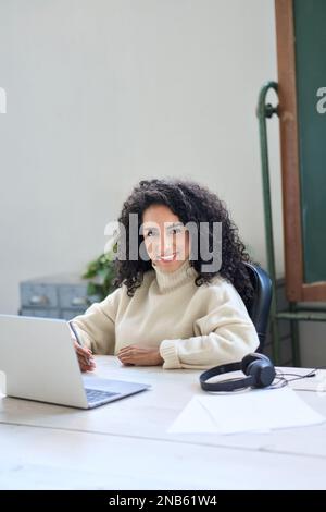 Junge, lächelnde Mitarbeiterin, die mit einem Laptop am Schreibtisch sitzt. Vertikales Hochformat Stockfoto