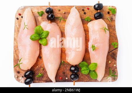 Rohes Hähnchenfleisch auf Spießen mit Oliven mit Gewürzen, Kräutern auf weißem Hintergrund. Ungekochtes Hähnchenfleisch, Kebab auf Spießen. Spieße von rohem Fleisch und Stockfoto