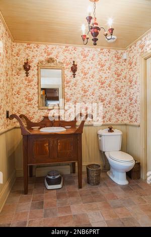Antiker Holzwaschtisch und weiße Porzellantoilette im Gäste-Waschraum mit Keramikfliesenboden im alten 1826 Landhausstil Feldsteinhaus. Stockfoto