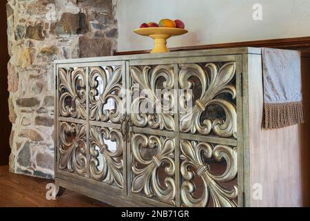 Bronzefarbenes antikes Holzbuffet mit Spiegeln und geschnitzten Fleur-de-Lis-Designs im Wohnzimmer im alten Landhaus aus dem Jahr 1826. Stockfoto