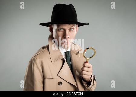 Männlicher Detective mit Lupe auf grauem Hintergrund Stockfoto