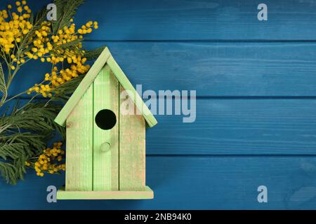 Wunderschönes Vogelhaus und Mimosablumen auf blauem Holztisch, flach liegend. Platz für Text Stockfoto