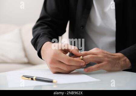 Ein Mann, der den Ehering am Tisch abnimmt. Scheidungskonzept Stockfoto