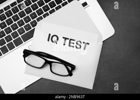 Papier mit den Worten IQ Test in Umschlag, Brille und Laptop auf schwarzem Tisch, flach liegend Stockfoto