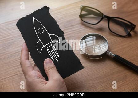 Ein Hand-Papier mit einem Raketensymbol mit Lupe und Glas auf der Rückseite. Stockfoto