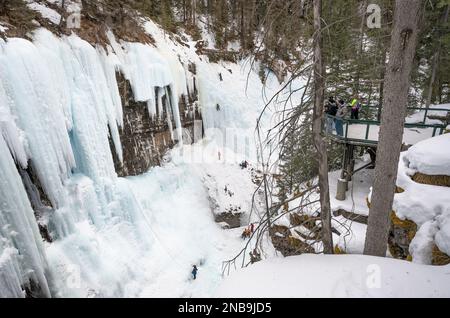 Banff National Park, Alberta, Kanada – 12. Februar 2023: Menschen auf einer Aussichtsplattform beobachten Eiskletterer auf einem gefrorenen Wasserfall im Johnston Canyon Stockfoto