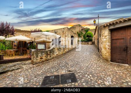 Das mittelalterliche spanische Dorf Pals, Spanien, mit einem Straßencafé auf seinen kopfsteingepflasterten, feuchten Straßen nach einem Sommerregen in der Nähe der Küste der Costa Brava. Stockfoto