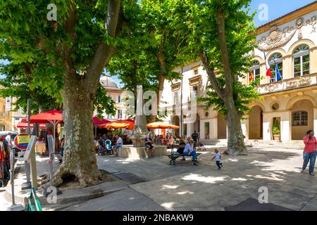 Eine der vielen typischen Straßen und kleinen Plätze mit Cafés und Geschäften in der historischen Stadt Saint-Remy-de-Provence an einem sonnigen Sommertag. Stockfoto