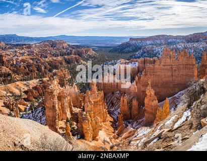 Der Bryce Canyon ist mit frisch gefallenem Schnee und fernen Bergen und leuchtend farbigen orangefarbenen Klippen geschmückt. Stockfoto