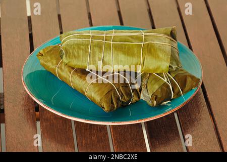 Umhüllt von Hallaca oder Tamale über einem rustikalen Tisch und einem blauen Gericht, mexikanische und venezolanische traditionelle Speisen Stockfoto