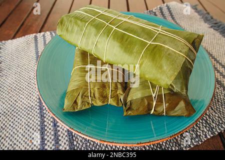 Umhüllt von Hallaca oder Tamale über einem rustikalen Tisch und einem blauen Gericht, mexikanische und venezolanische traditionelle Speisen Stockfoto