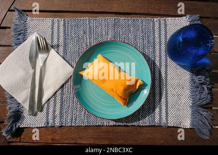 Hallaca oder Tamale bei einem rustikalen Tisch und einem blauen Gericht mit einem Getränk, mexikanischen und venezolanischen traditionellen Speisen Stockfoto