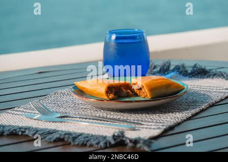 Hallaca oder Tamale über einem rustikalen Tisch und einem blauen Gericht mit einem Getränk, mexikanische und venezolanische traditionelle Speisen mit einem Hintergrund aus Miami, Florida Stockfoto