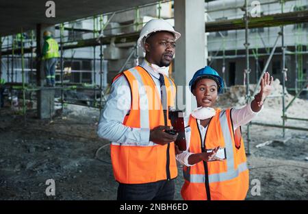 Ein gut gebautes Gebäude erfordert einen gut durchdachten Plan. Ein junger Mann und eine junge Frau, die sich auf einer Baustelle unterhalten. Stockfoto