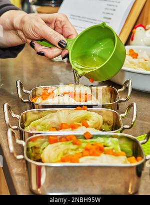 Der Koch gießt Sauce auf Kohlbrötchen mit Lachs und Karotten in der Küche. Französisches Rezept Stockfoto