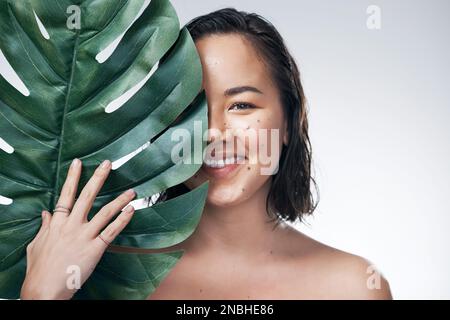 Pflegen Sie Ihre Haut auf natürliche Weise. Studioaufnahme einer wunderschönen jungen Frau, die ein Monsterblatt gegen ihr Gesicht hält. Stockfoto
