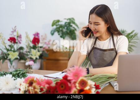 Blumengeschäft Konzept, weibliche Floristin im Gespräch mit dem Kunden auf dem Smartphone und notieren auf Notebook. Stockfoto