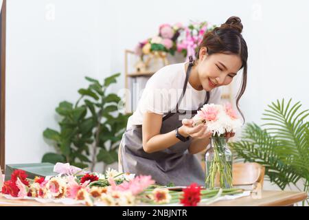 Blumenladen-Konzept, weiblicher Blumenhändler lächelt und riecht nach bunten Blumen in Vase mit Glück. Stockfoto