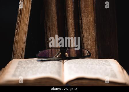 Eine offene verschwommene Seite mit hebräischem religiösen Text, Brille und alten, schäbigen jüdischen Büchern mit Lederbindung Chumash im Hintergrund. Ich Studiere Torah Stockfoto