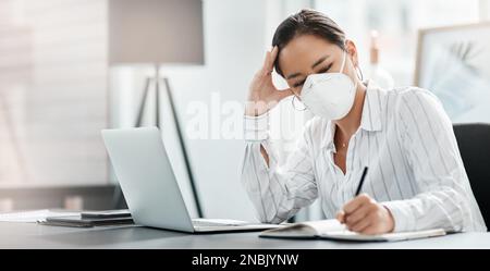 Die Moral schwindet, wenn man sich eingesperrt fühlt. Eine maskierte junge Geschäftsfrau, die gestresst wirkt, während sie an ihrem Schreibtisch in einem modernen Büro arbeitet. Stockfoto